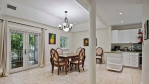 A spacious dining area with a large table and chairs, a chandelier, and a view of the outdoors through sliding glass doors. - Spacious 3 BR Townhouse w/ Infinity Pool Views (Nassau)