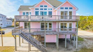 A two-story pink house with a balcony and a wooden staircase leading to the upper level. - Oceanview Home w/ Private Pool, Hot Tub, Game Room, Theater, and Volleyball (Waves)
