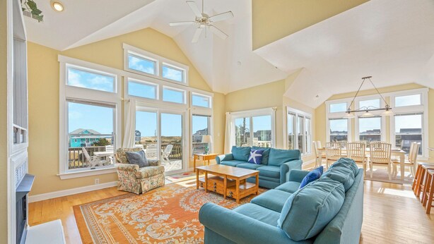 A spacious living room with a large sofa, a coffee table, and a view of the beach through large windows. - Oceanview Home w/ Private Pool, Hot Tub, Game Room, Theater, and Volleyball (Waves)