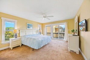 A bedroom with a bed, two bedside tables, a ceiling fan, and a view of a balcony.