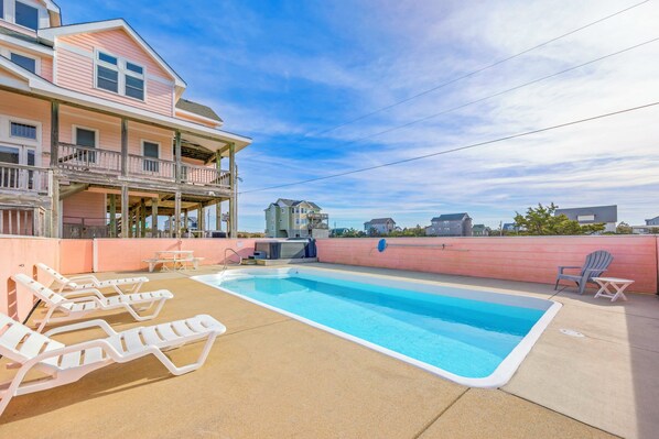 A swimming pool with lounge chairs, a covered deck, and a building with a balcony.