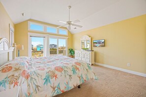 Ein Schlafzimmer mit Bett, Kommode, Deckenventilator, Fenster und Blick auf Häuser.