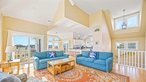 A spacious living room with two blue sofas, a wooden coffee table, and a patterned rug. - Oceanview Home w/ Private Pool, Hot Tub, Game Room, Theater, and Volleyball (Waves)