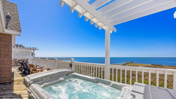 Un jacuzzi con vista despejada al océano, una terraza de madera con sillones de descanso y una pérgola blanca.