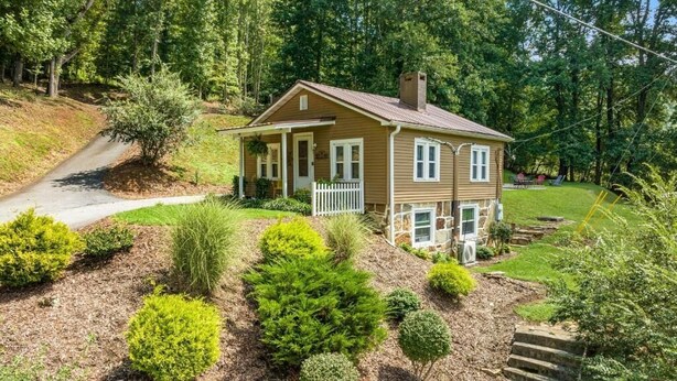 Una casa a due piani con un portico anteriore, circondata da un giardino curato con arbusti diversi e una recinzione in legno.