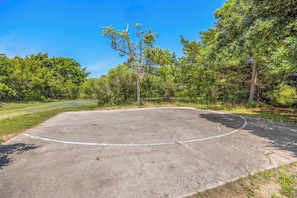 Ein Basketballplatz im Freien mit Korb, umgeben von Bäumen und Grünpflanzen.