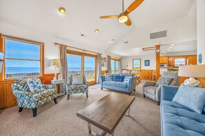 A spacious living area with a view of the ocean, wooden furniture, and a ceiling fan.