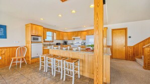 A modern kitchen with wooden cabinets, a central island with bar stools, and a microwave above the sink.