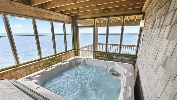 A wooden cabin with a hot tub overlooking a body of water.