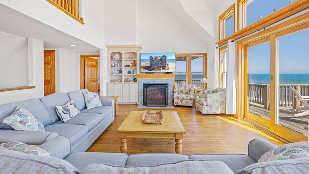 Een ruime woonkamer met een grote bank, een open haard en uitzicht op zee.