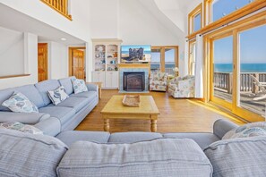 A spacious living room with a large sofa, a fireplace, and a view of the ocean. - Premier Oceanfront Dog Friendly w/ Pool, Hot Tub, EV Charger, Elevator, Theater (Rodanthe)