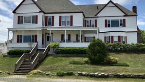 A two-story house with a front porch, a staircase leading to the entrance, and a small front yard with a tree and a stone wall. - Diane Cottage, York Manor, Short Sands Beach (York)