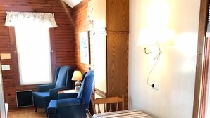 A cozy cabin interior with a dining table, chairs, a blue armchair, and a lamp. - Diane Cottage, York Manor, Short Sands Beach (York)