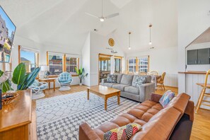 A spacious living room with a high ceiling, a sofa, a coffee table, and a dining area with chairs.