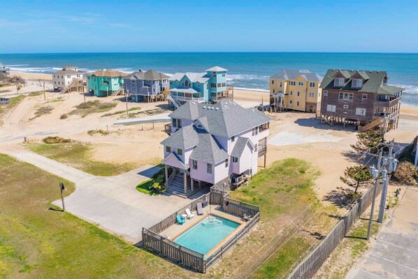 A beachfront property with a large house featuring a swimming pool, multiple decks, and ocean views.