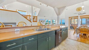 A modern kitchen with a wooden countertop, dark cabinets, and a view to the outside. - Semi-Oceanfront Dog Friendly Home w/ Private Pool, Hot Tub, Foosball, Basketball (Rodanthe)
