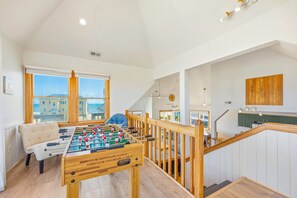 A spacious room with a foosball table, a sofa, and a view of the sea.