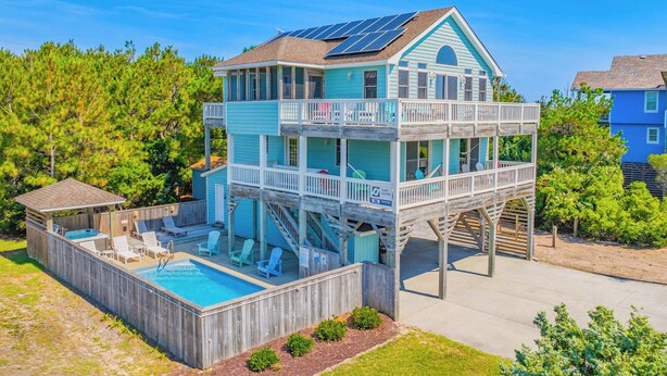 Una casa de varios pisos con piscina, terraza de madera y paneles solares.