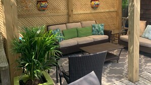A covered patio area with a wooden pergola, a cushioned sofa, wicker chairs, and a potted plant. - Beautiful Ocean Park Family Vacation Rental (Ocean Bay Park)