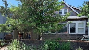 A house with a stone retaining wall, a large tree, and a wooden deck. - Beautiful Ocean Park Family Vacation Rental (Ocean Bay Park)