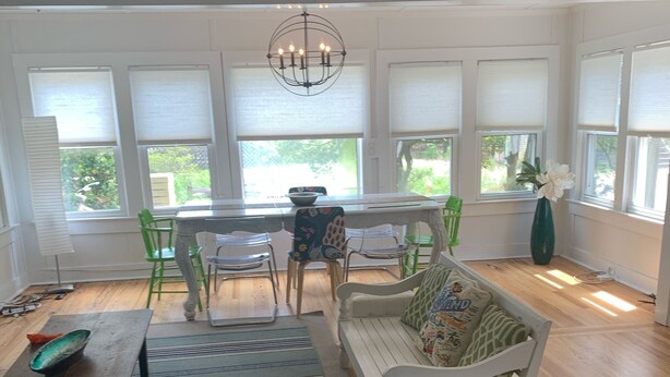 A spacious living room with a wooden floor, a dining table with chairs, a sofa, and a chandelier. - Beautiful Ocean Park Family Vacation Rental (Ocean Bay Park)
