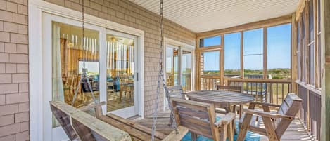 A covered outdoor area with a table and chairs, a swing, and a view of the beach.
