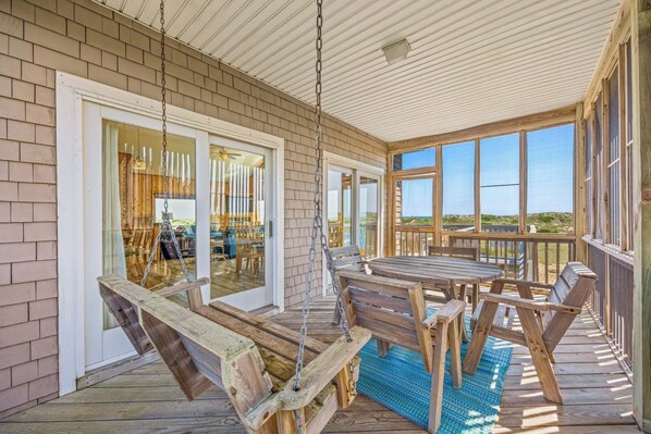A covered outdoor area with a table and chairs, a swing, and a view of the beach.