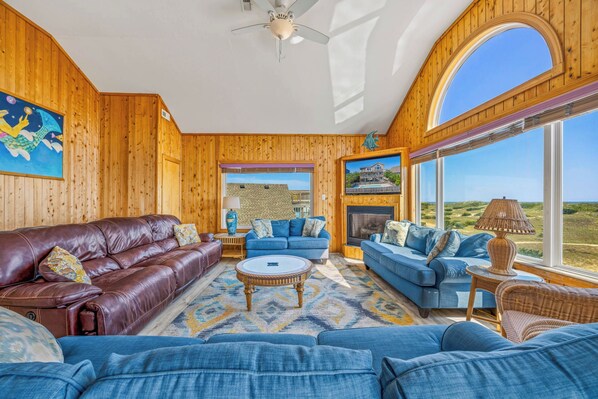 A spacious living room with a fireplace, leather sofas, and large windows offering a view of the landscape.