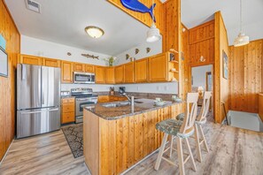A kitchen with wooden cabinets, stainless steel appliances, a granite countertop, and a bar area with stools. - Oceanfront Dog Friendly Home in Salvo w/ Private Pool, Hot Tub, and Game Room (Salvo)