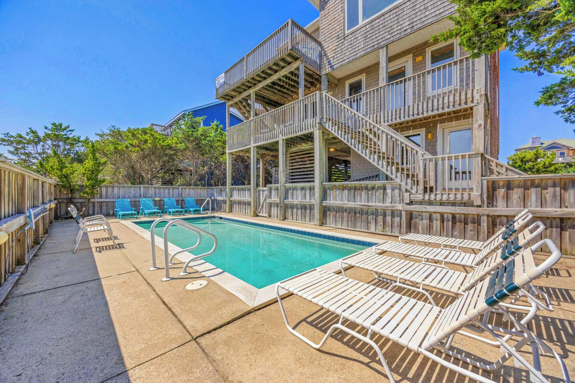 A pool area with a wooden deck, lounge chairs, and a staircase leading to an upper level.