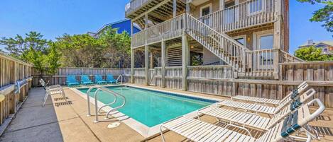 A pool area with a wooden deck, lounge chairs, and a staircase leading to an upper level.