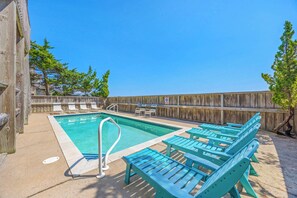 A swimming pool with lounge chairs, a wooden fence, and trees in the background.