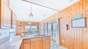 A modern kitchen with wooden cabinets, a central island, and a large window offering a view. - Oceanfront Dog Friendly Home in Salvo w/ Private Pool, Hot Tub, and Game Room (Salvo)