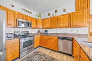 A kitchen with wooden cabinets, stainless steel appliances, and decorative fish wall art. - Oceanfront Dog Friendly Home in Salvo w/ Private Pool, Hot Tub, and Game Room (Salvo)
