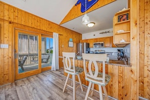 A wooden interior with a kitchen area, two bar stools, and a sliding glass door leading to an outdoor deck.