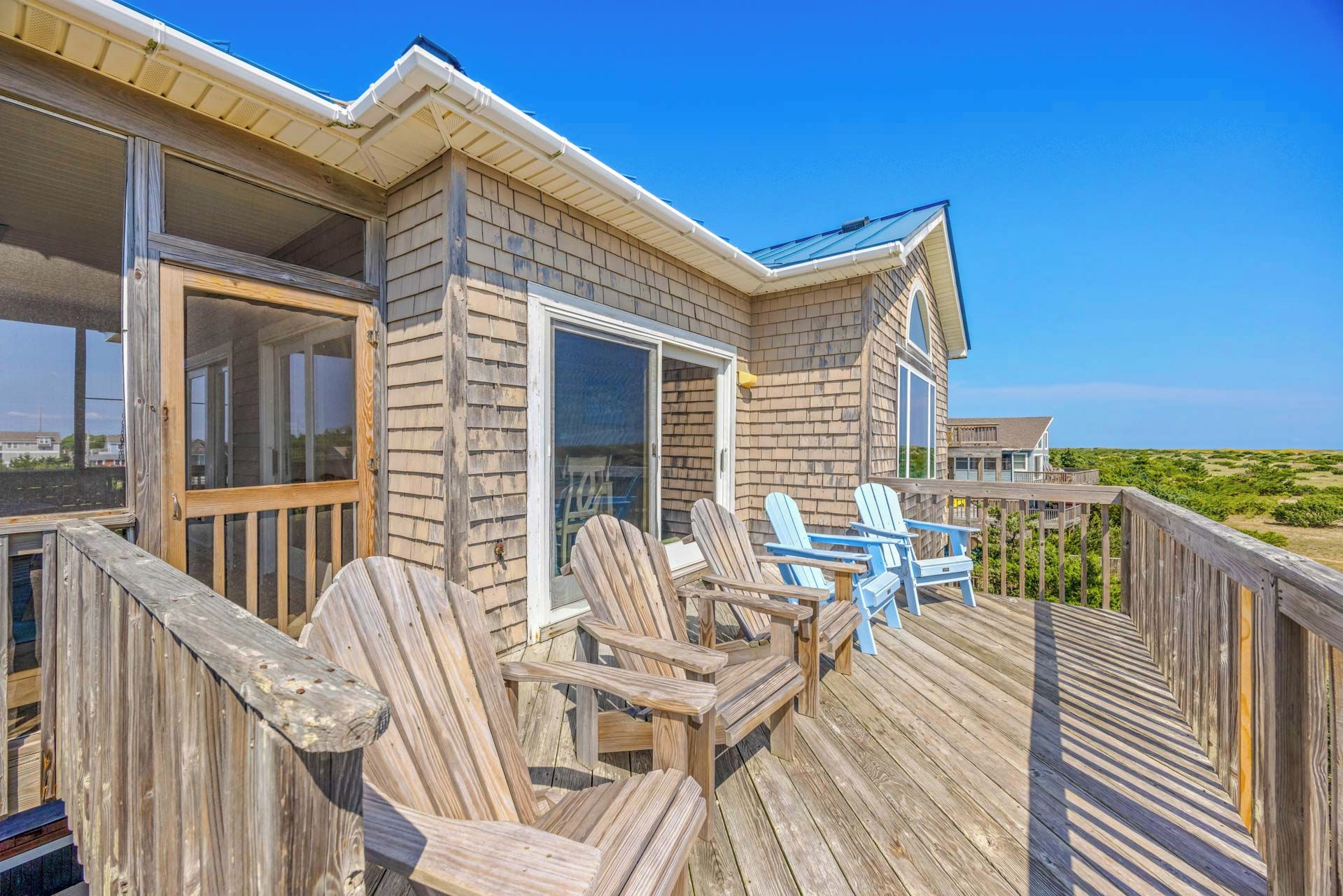 A wooden deck with Adirondack chairs, a glass door entrance, and a view of the beach.
