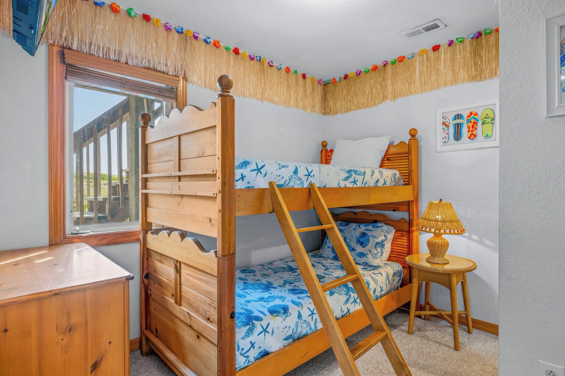 A bunk bed room with a window, a small table, and a wall decoration.