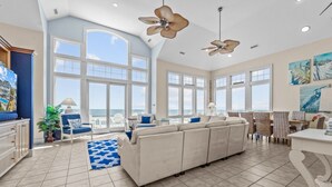 A spacious living room with a large sofa, two ceiling fans, and a view of the ocean through large windows. - Premier Oceanfront Dog Friendly w/ Pool, Elevator, Hot Tub, Theater & Game Rooms (Hatteras)