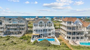 A coastal residential area with multiple two-story houses featuring balconies and a swimming pool. - Premier Oceanfront Dog Friendly w/ Pool, Elevator, Hot Tub, Theater & Game Rooms (Hatteras)