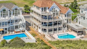 A coastal residential complex with multiple houses featuring balconies, swimming pools, and outdoor seating areas. - Premier Oceanfront Dog Friendly w/ Pool, Elevator, Hot Tub, Theater & Game Rooms (Hatteras)