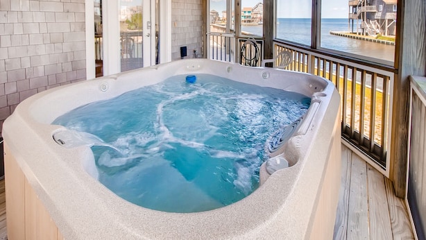 Ein Whirlpool auf einer Holzterrasse mit Blick auf das Meer und Gebäude.