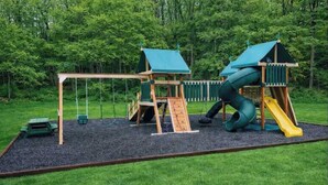 A playground with two play structures, a slide, and a swing set. - Cabin w/ gas fireplace, playground& AuTrain Lk Access (AuTrain)