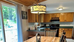 A wooden dining table with chairs, a hanging light fixture, and wooden cabinets in a kitchen. - Cabin w/ gas fireplace, playground& AuTrain Lk Access (AuTrain)