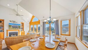 Un vaste espace dédié à la salle à manger, avec une longue table en bois, des sièges confortables et de grandes fenêtres offrant une vue sur les environs.