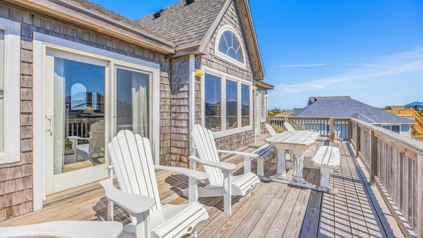 Une terrasse en bois avec des fauteuils Adirondack, un espace salon couvert et une grande fenêtre donnant sur l’océan.