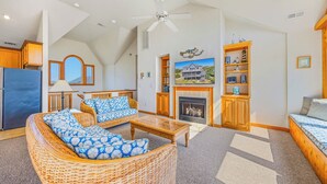 Un salon spacieux avec un haut plafond, une cheminée, une grande fenêtre et une vue sur une maison.