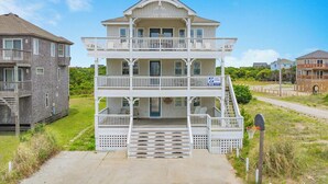A two-story beachfront house with a balcony, a porch, and a staircase leading to the entrance. - Semi-Oceanfront Dog Friendly Home w/ Pool, Hot Tub, Renovated Kitchen, Game Room (Hatteras)