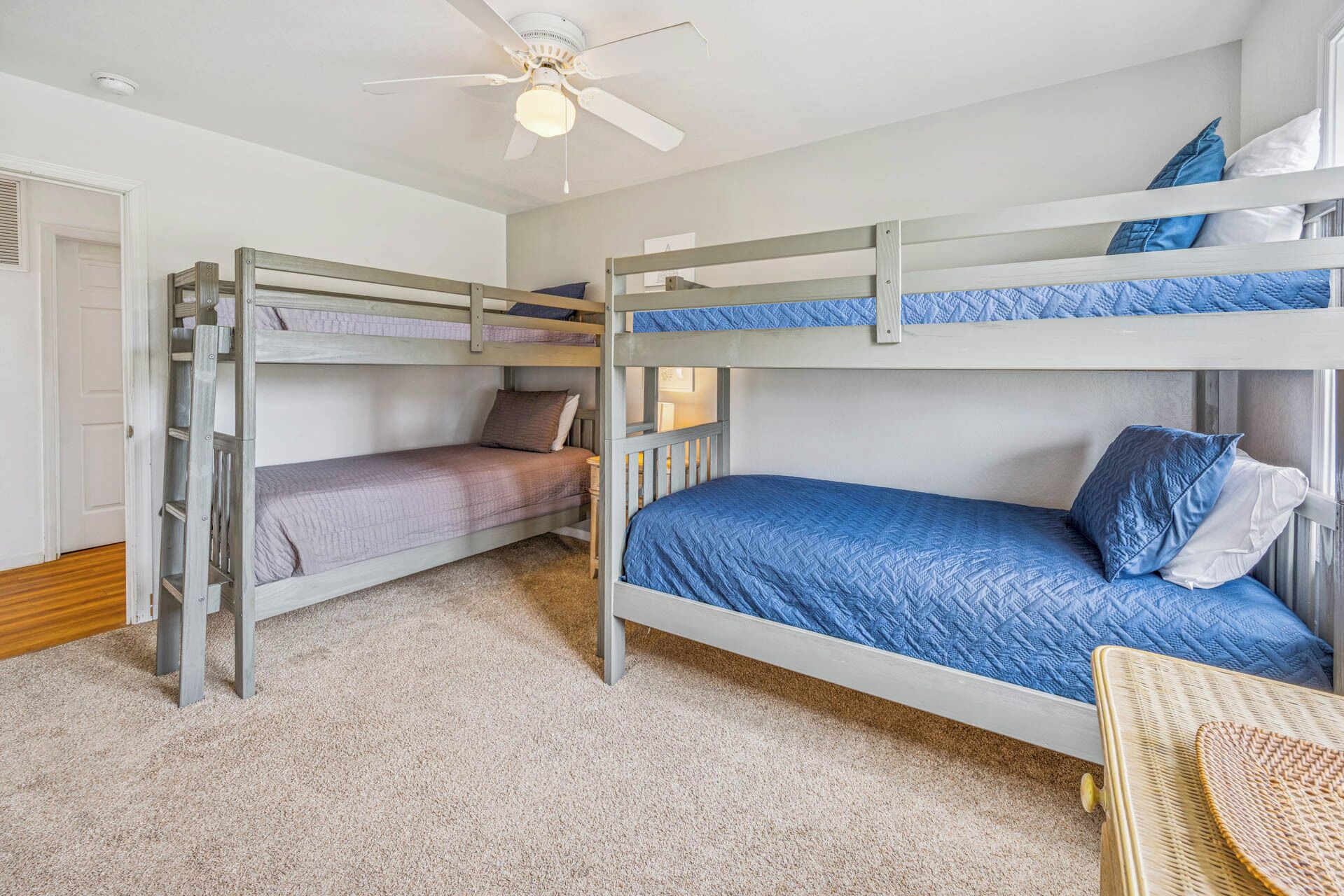 A bunk bed room with a ceiling fan, carpeted floor, and a wicker chair.