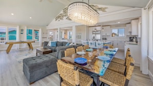 A spacious living room with a large dining table, grey sofas, and wicker chairs. - Oceanfront Dog Friendly Home with Private Pool, Hot Tub, Direct Beach Access (Avon)