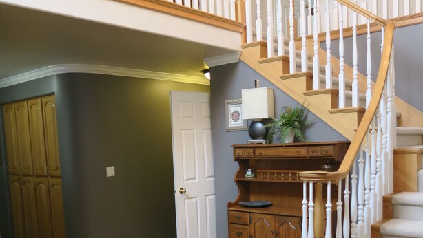 A spacious foyer with a wooden staircase, a large rug, and a built-in cabinet.